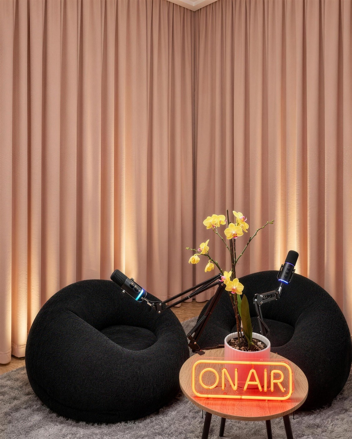 Set de podcast con dos puffs negros, micrófonos, orquídea amarilla y neón ON AIR frente a cortina rosada