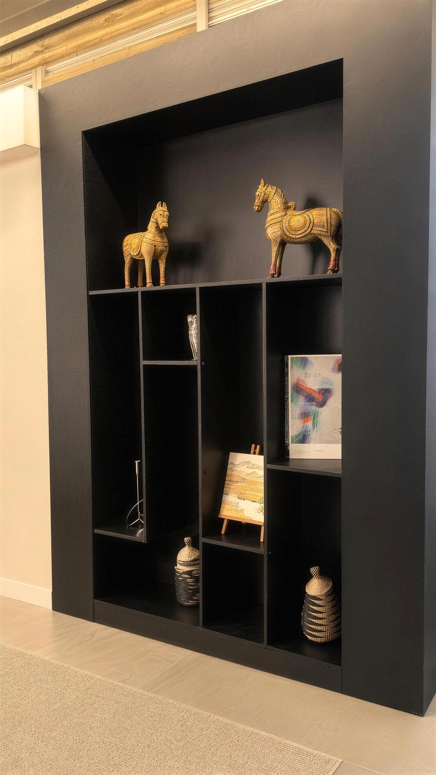 Mueble negro con caballos de madera, libros y objetos decorativos